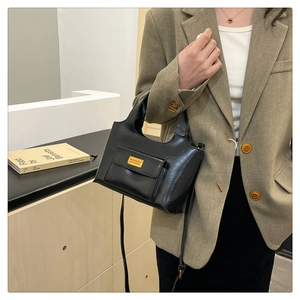 Détail du sac à main noir brillant avec poche frontale à rabat et plaque en métal doré