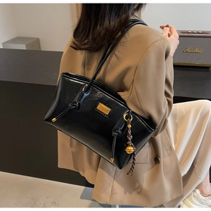 Detail shot of black patent leather tote bag featuring gold hardware and side knot charm