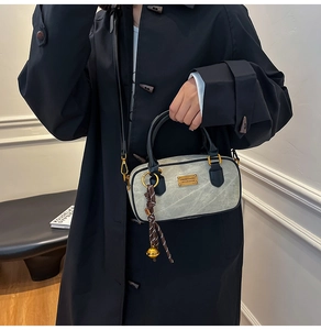 Detail of grey stone textured crossbody bag with gold hardware and bell charm