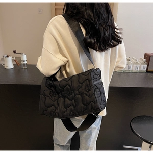 Detail of quilted floral pattern on black canvas crossbody bag worn by a model
