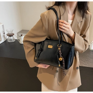 Detail of black leather tote bag with gold logo and woven charm on camel blazer outfit