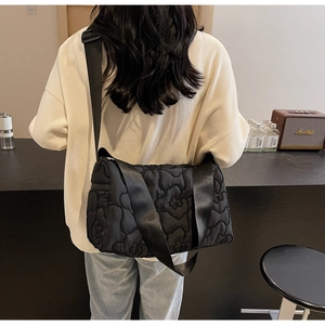 Detail of black quilted shoulder bag with wave patterns and wide adjustable strap on model