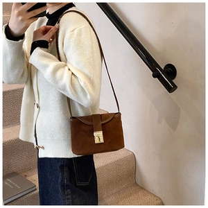 Brown frosted suede crossbody bag with gold buckle shown on a white knitted cardigan