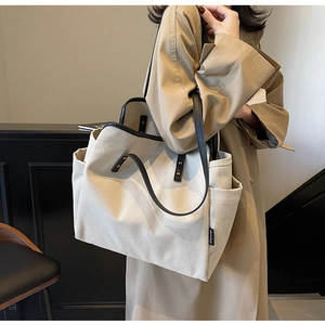 Close-up of beige canvas tote bag with black contrast trim and side pocket on model