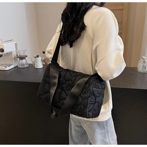 Close-up of black quilted shoulder bag featuring floral patterns and a wide fabric strap