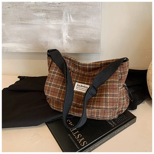 Detailed view of brown plaid tweed shoulder bag with woven strap on aesthetic background