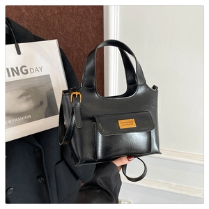Détail du sac seau vintage en cuir noir avec logo en métal doré et rabat à boucle aimantée