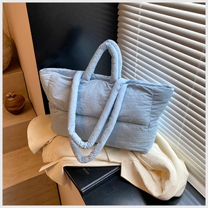 Detail of light blue quilted puffer tote bag with dual straps on white blazer