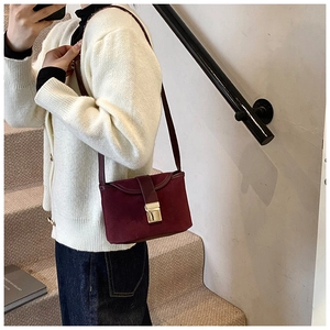Detail of burgundy matte leather crossbody bag with gold buckle on a stylish model