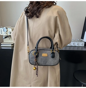 Macro shot of dark grey matte handbag with gold metal plate and bell pendant detail