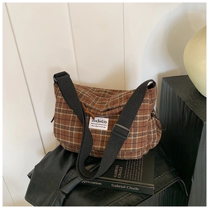Close-up of brown plaid canvas shoulder bag with adjustable strap and retro logo detail
