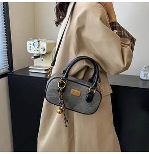 Detail of dark grey cylindrical crossbody bag with gold hardware and bell charm
