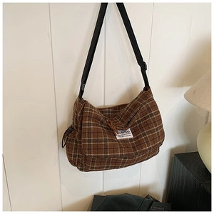 Detail of brown plaid crossbody bag texture and adjustable strap on a wooden wall