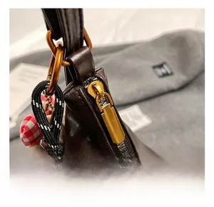 Close-up of vintage brass zipper, D-ring, and plush woven bag pendant on dark brown leather