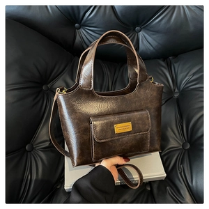 Détail d'un sac en cuir marron vintage avec plaque en métal doré et texture de grain fin