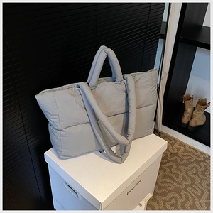 Detailed view of light gray quilted puffer tote bag on a white minimalist storage box