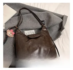 Detail of dark brown faux leather hobo bag with a plush bear charm on soft fabric