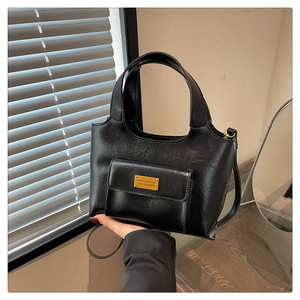 Détail du sac cabas noir avec finition brillante et plaque logo en métal doré décorative