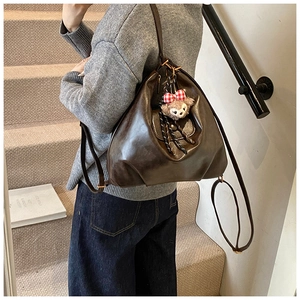Detail of a brown oil-wax PU leather backpack showing a plush bear charm on a soft bag