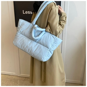 Close-up of light blue quilted puffer tote bag with thick soft handles on model shoulder