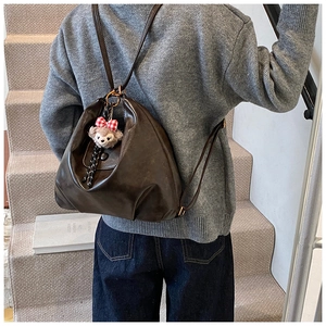 Detail of dark brown vintage leather backpack with a plush bear charm on side pocket