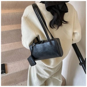 Detail of black bowling pillow bag with dual straps and mini coin purse charm on model