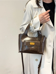Sac seau vintage en cuir PU marron avec poignée et plaque dorée porté sur un trench-coat