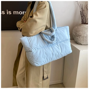 Detailed side view of a light blue quilted puffer tote bag on a fashion model