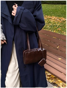 Detail view of brown rectangle shoulder bag with smooth leather texture on a wooden bench