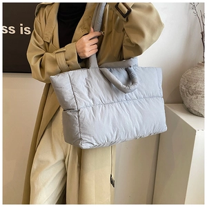 Light grey quilted down tote bag carried over shoulder by a model in a modern home setting