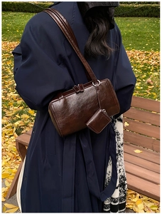 Detail of dark brown polished leather cylinder bag with mini coin purse on a blue coat