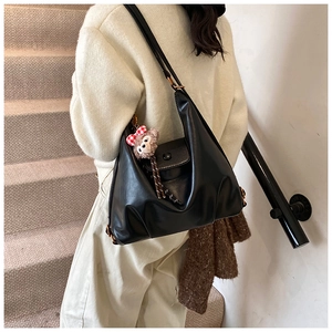 Close-up of black synthetic leather hobo bag with a cute plush bear charm on a strap