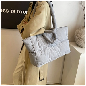 Detailed view of the large quilted puffer tote bag in grey blue worn by a model