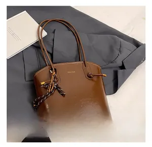 Détail d'un sac cabas en cuir marron brillant avec nœud latéral et logo métallique