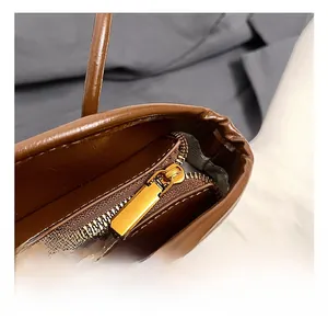 Détail du sac en cuir marron foncé montrant la fermeture éclair dorée et les coutures