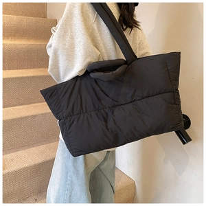 Close-up of black quilted puffer tote bag shown on model with shoulder strap detail