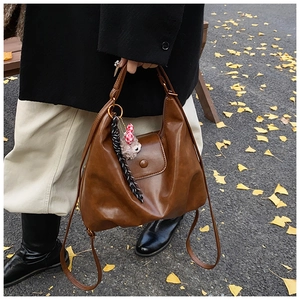Detail of dark brown leather handbag with plush charm and striped ribbon in autumn setting