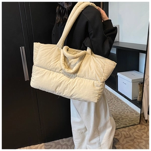 Detailed view of the large beige quilted down puffer tote bag on a model's shoulder