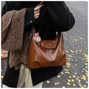 Brown vintage leather hobo bag with hedgehog charm and silk scarf on autumn street