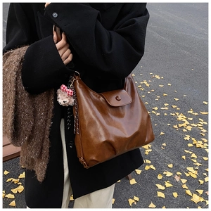 Brown vintage faux leather shoulder bag with plush charm on ginkgo leaf background