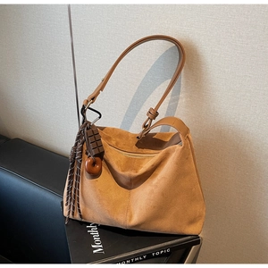 Brown suede underarm bag with wide strap and decorative chocolate donut charms on sofa