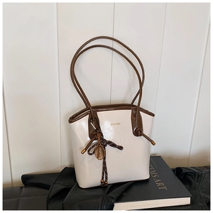 Détail d'un sac cabas crème avec finitions en cuir marron et pendentif de tennis chic