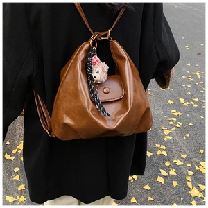 Brown PU leather backpack with plush bear charm shown in an autumn street scene