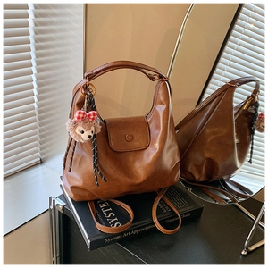 Detailed view of brown retro leather handbag with plush bear charm and adjustable strap