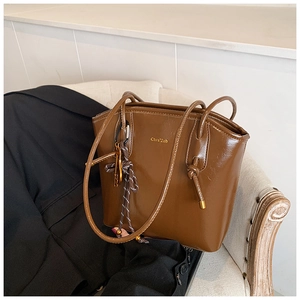 Détail d'un sac seau marron brillant avec logo et charme en corde tressée sur sofa