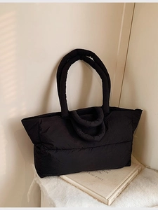 Puffy black quilted down tote bag with dual shoulder straps on a minimalist background
