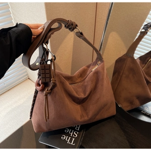 Detailed close-up of dark brown suede hobo bag with wide strap and designer charms