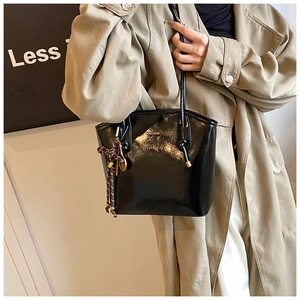 Gros plan du sac seau en cuir verni noir avec logo doré et détail de nœud à pois