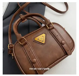 Close-up of golden triangular logo and vintage brown PU leather texture on a Boston bag