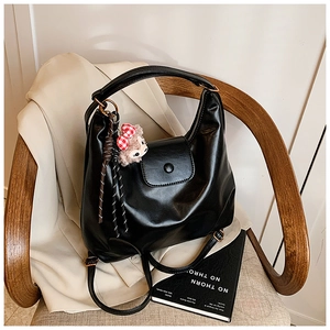 Detailed view of black faux leather multipurpose backpack with plush bear charm on wood chair